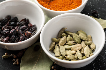 Barberry, cardamon berries and paprika in white ceramic bowls on a black wooden table, closeup shot