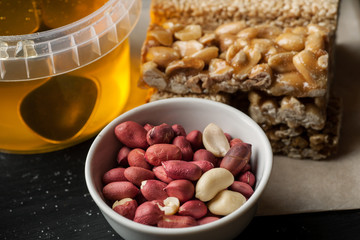 Raw peanuts in ceramic bowl and honey jar on a black wooden table