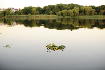 Wreaths of wild flowers float on the river against the backdrop of sunset and nature