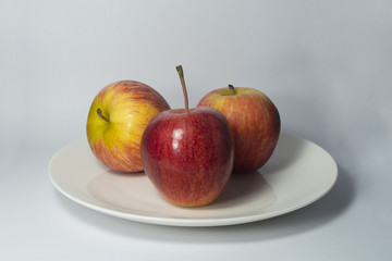 Tres manzanas en un plato blanco con fondo degradado gris