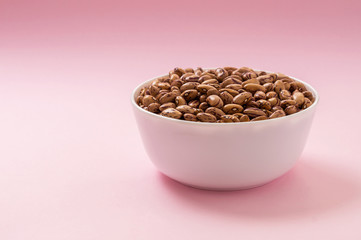Raw pinto bean in a bowl on pink background