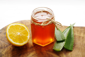 Honey in a glass jar, lemon and aloe vera on a wooden board on a white background. Alternative medicine