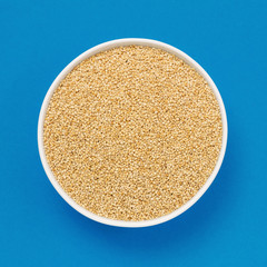 Raw white quinoa in a bowl on blue background