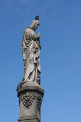 Fototapeta na wymiar Maria sculpture of stone with a dove on the head, Mary's column from Kaspar von Zumbusch 1861 in Paderborn, blue sky with copy space