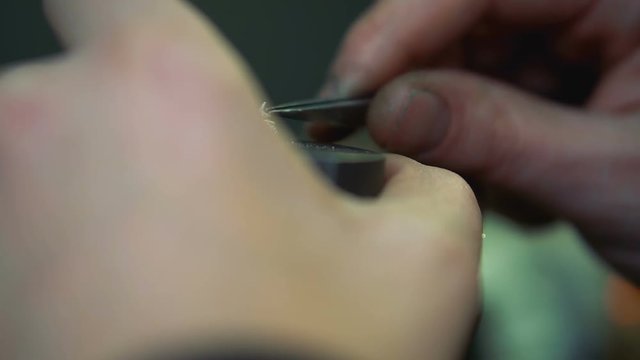 Jeweler takes gem using forceps and insert it into the silver ring close-up