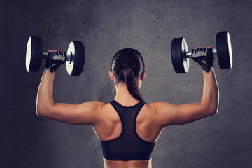 Obraz premium young woman flexing muscles with dumbbells in gym