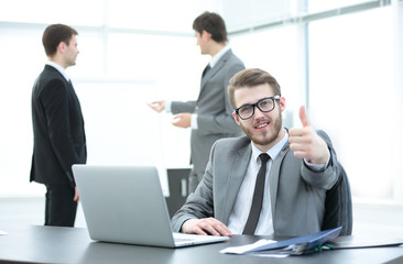 Manager sits at a Desk with an open laptop and showing thumbs up