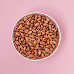 Raw pinto bean in a bowl on pink background