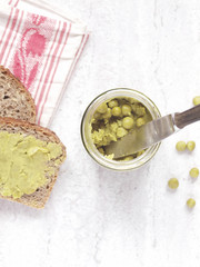 Green peas paste in a jar next to slices of wholegrain bread and kitchen cloth