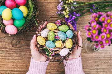 Woman hands holding painted easter egg in a small nest. Toned picture. Top view. Selective focus.