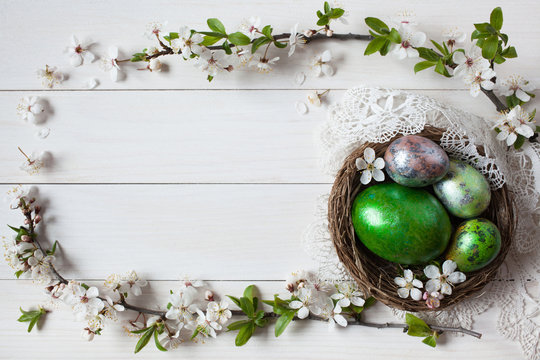 Easter white wooden background with a nest, eggs and branch with flowers, space for text greeting