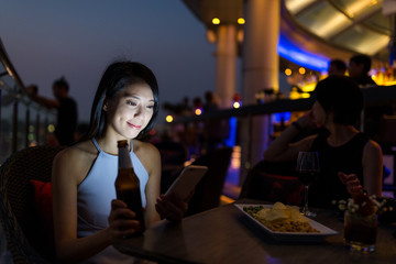 Woman enjoy her beer and using cellphone at night
