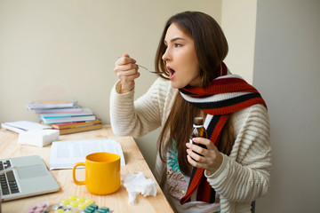 Girl with a scarf on taking medicine. Ill student drinking cough syrup for treatment
