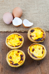 Few egg tarts on wooden table with chicken egg and egg shells