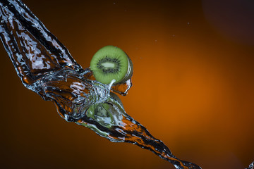 two halves of kiwi and splash of water on orange background