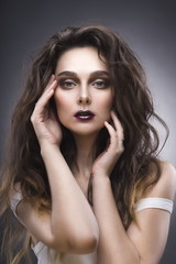 beauty portrait of the young woman in a white undershirt with a vanguard make-up and a flowing hair on a gray background