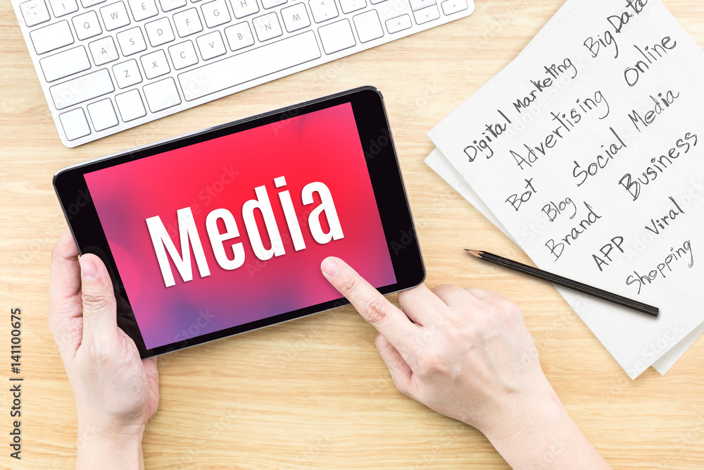 Poster Hand using tablet with Media word on screen with list of digital marketing features on paper on work table,Online business concept
