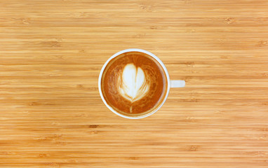 Top view of a coffee with heart pattern in a white cup on bamboo wooden background