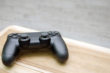 Video game controller on wooden desk with brick  wall background, copy space for text, color tone...