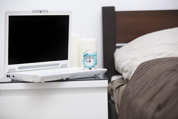 cool laptop, alarm clock and candles on the table near bed in the cozy bedroom