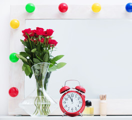 bunch of roses in vase, alarm clock, bottle of perfume and founfation on the wonderful mirror with lights background