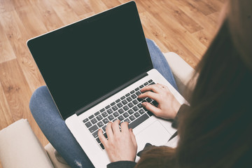 Fototapeta premium The young woman is sitting on the sofa and working at laptop