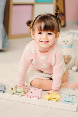 cute happy 2 years old baby girl playing with toys at home. Modern nursery interior in pastele tones, early learning concept
