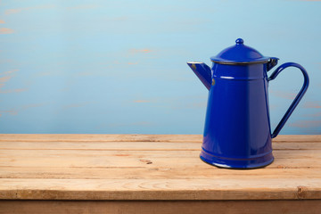 Vintage enamel coffee pot on wooden table over painted wall background