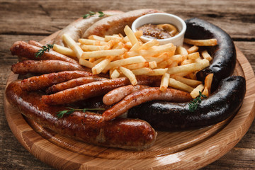 Traditional Oktoberfest menu. Various sausages served with sauce and french fries on wooden table, close up