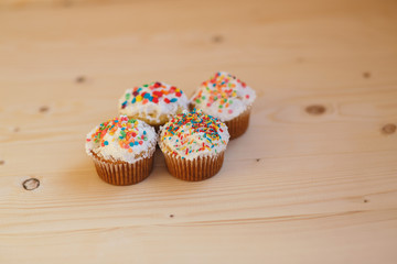 Easter cupcakes with cream and small confetti on a wooden table. Spring.