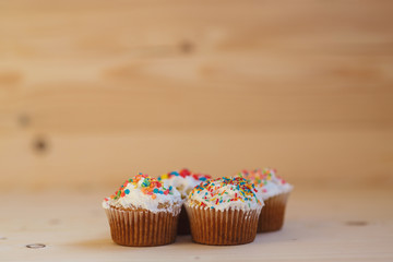 Easter cupcakes with cream and small confetti on a wooden table. Spring.