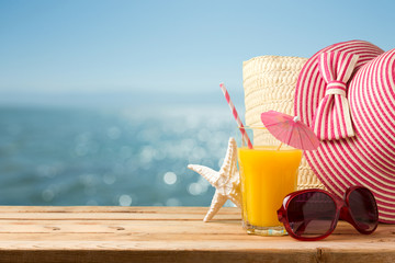 Summer holiday vacation concept with orange juice, hat and sunglasses over sea beach background