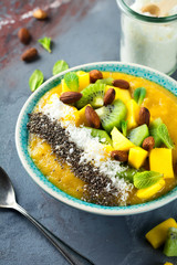 Mango smoothie bowl with pieces of kiwi, mango, coconut shavings and chia seeds on a stone background. Selective focus.