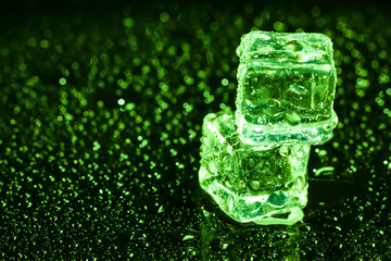 Ice cubes in green light on black wet table.