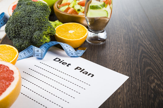 Food and sheet of paper with a diet plan on a dark wooden table.