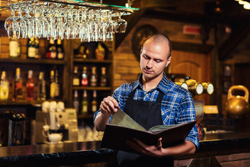 Barman at work in pub,Portrait of cheerful barman worker standing,Waiter giving menus,A pub.Bar.Restaurant.Classic.Evening.European restaurant.European bar.American restaurant.American bar.