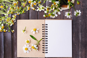 Blank notebook with white flower and bas ket of flower on vintage wooden table View from above with copy space