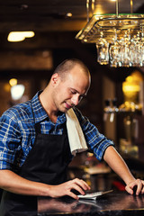 Barman at work in pub,Portrait of cheerful barman worker standing,Waiter giving menus,A pub.Bar.Restaurant.Classic.Evening.European restaurant.European bar.American restaurant.American bar.