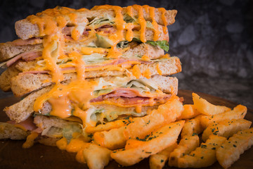 Sandwich with spicy sauce and French fries on wood plate.