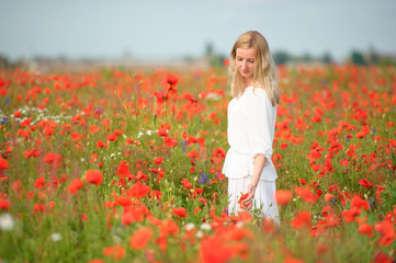 Fototapeta na wymiar Woman wearing white dress plying with red flowers in blooming summer field