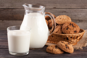 jug and glass of milk with oatmeal cookies in a wicker basket on a wooden background