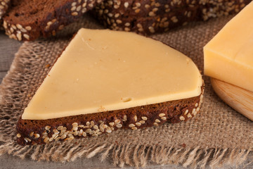 slices of black bread with sesame seeds and cheese on the old wooden background