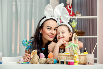 Happy easter! A mother and her daughter painting Easter eggs. Happy family preparing for Easter. Cute little child girl and mom wearing bunny ears on Easter day.