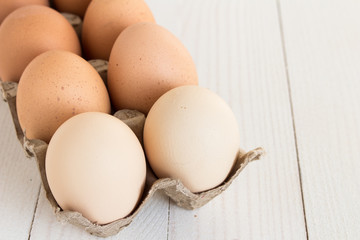 Fresh eggs in carton package on white wood background