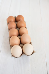 Fresh eggs in carton package on white wood background
