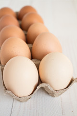 Fresh eggs in carton package on white wood background