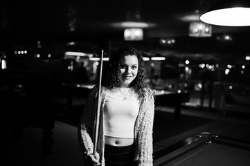 Young curly girl posed near billiard table. Sexy model at black mini mini skirt play russian snooker. Play game and fun concept.