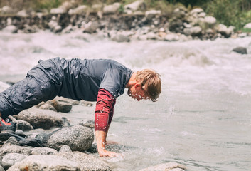 Traveler man washes his face with cold water in mountain river