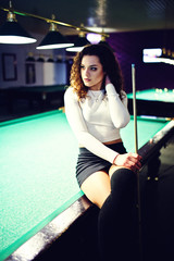 Young curly girl posed near billiard table. Sexy model at black mini mini skirt play russian...