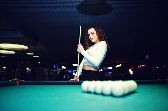 Young curly girl posed near billiard table. Sexy model at black mini mini skirt play russian snooker. Play game and fun concept.